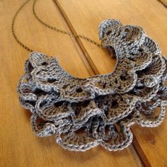 a crocheted necklace is sitting on a wooden surface with a chain attached to it