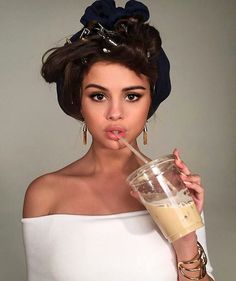 a woman drinking from a straw in her hand while wearing a white top and gold hoop earrings