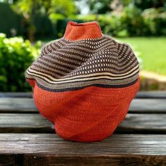 an orange vase sitting on top of a wooden table next to a green grass field