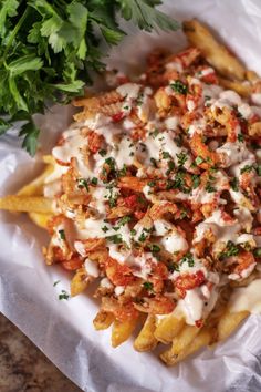 french fries covered in sauce and parsley on top of a white paper wrapper