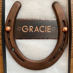 a horseshoe with the word grace written on it and two hearts in the center, hanging from a wooden frame