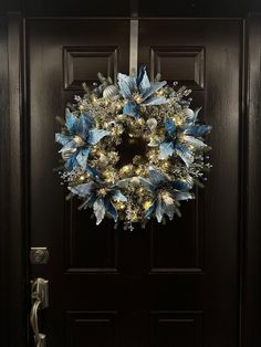 a wreath on the front door of a house decorated with blue flowers and lights for christmas