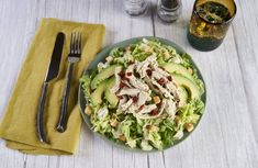 a salad with chicken, avocado and cranberries in a bowl next to a fork