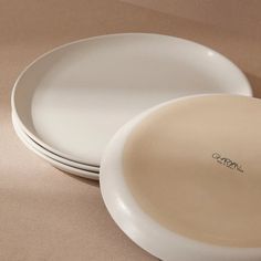 three white plates sitting next to each other on top of a brown tablecloth covered surface