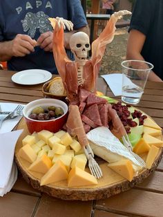 a skeleton sitting on top of a wooden plate filled with cheese and meat