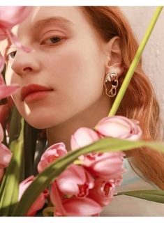 a woman with long red hair wearing pink flowers in front of her face and behind her ear