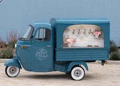 a small blue truck with flowers on the back and an ice cream cart behind it