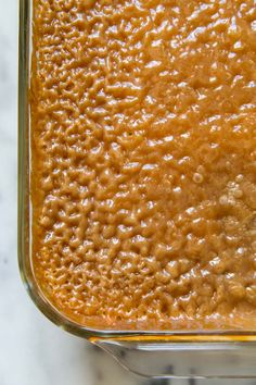 a glass dish filled with brown sauce on top of a white marble countertop next to a knife