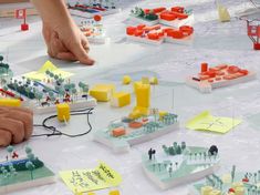 a group of people playing with legos and paper buildings on a table together,