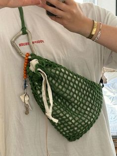 a woman holding a cell phone in her hand and wearing a green netted bag