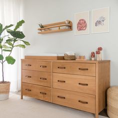 a wooden dresser sitting in a living room next to a potted plant and two pictures on the wall