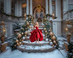 a woman in a red dress standing on the steps of a house decorated for christmas