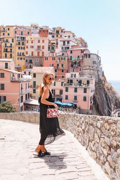 a woman walking down a stone walkway next to the ocean with buildings in the background