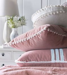 pink pillows stacked on top of each other in front of a white dresser and lamp