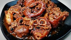 a black plate topped with meat and onions covered in brown sauce on top of a white table