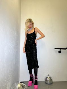 a woman in black dress and pink boots standing next to mirror ball on the floor