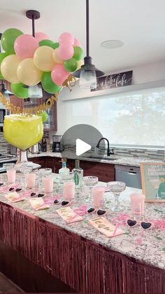 a table topped with lots of pink and green balloons next to a counter covered in food