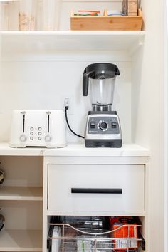 a blender sitting on top of a white shelf next to a toaster oven