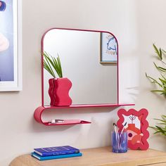 there is a mirror on the wall next to a desk with a vase and books