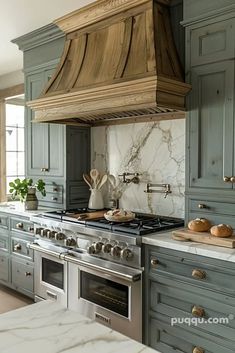 a kitchen with green cabinets and marble counter tops, an oven hood over the stove