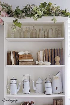 an old book shelf with books and vases on it, along with other antique items