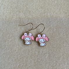 pair of pink and white cartoon character earrings on beige carpeted surface with light brown background