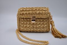 a straw purse with tassels and a gold chain on the bottom, sitting on a white surface