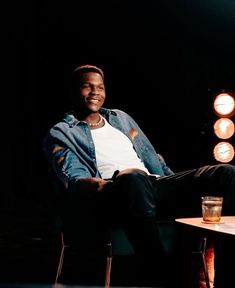 a man sitting in a chair next to a table with a glass on top of it