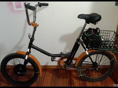 an orange and black bicycle parked in front of a white wall with a basket on it