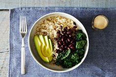 a white bowl filled with rice, beans and greens next to a glass of milk