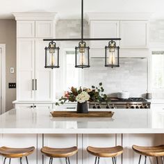 a kitchen island with four stools in front of it and lights hanging from the ceiling