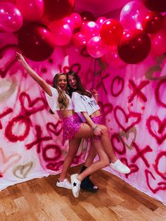 two young women posing in front of a backdrop with red and pink balloons on it