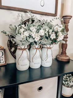 three mason jars with flowers in them are sitting on a table next to a framed sign