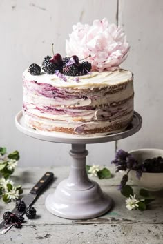 a cake with berries and flowers on top is sitting on a table next to other desserts