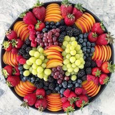 a platter filled with assorted fruit on top of a marble countertop next to sliced strawberries, grapes, and peaches