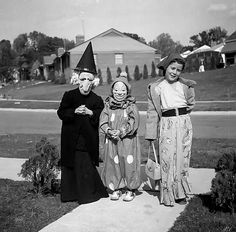 three women in halloween costumes standing next to each other on a sidewalk with houses in the background