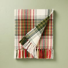 a plaid blanket hanging on the wall next to a white and green towel with tassels