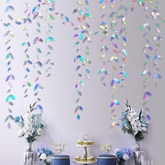 a table topped with blue chairs next to a wall covered in colorful paper leaves hanging from it's ceiling