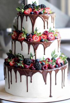 a three tiered cake with berries and chocolate drizzled on it's sides