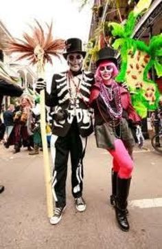 two people dressed up in skeleton costumes and holding a stick on a street with other people