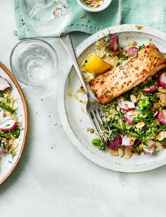 a white plate topped with fish next to a bowl of salad and a glass of water