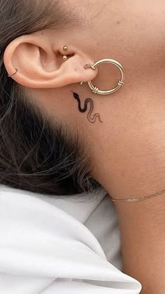 a woman wearing a gold ear cuff with a snake tattoo on her left behind the ear