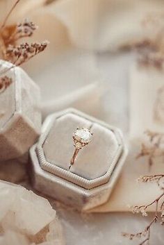 an engagement ring sits in a box next to some dried flowers and other jewelry items