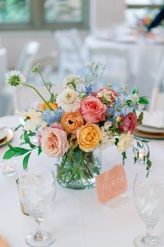 a vase filled with lots of flowers sitting on top of a table next to wine glasses