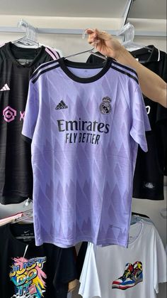 a person holding up a purple shirt in front of other soccer shirts and t - shirts