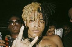 a shirtless man with dreadlocks holding up his peace sign in front of the camera