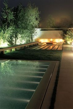 an outdoor swimming pool at night with lights shining on the water and trees in the background