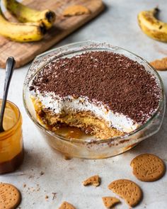 a dessert in a glass bowl with chocolate and vanilla toppings on the side next to some cookies