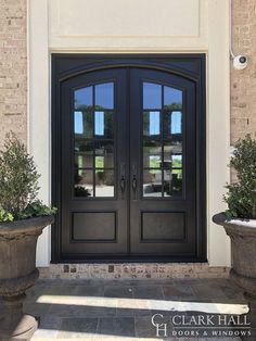 two planters on either side of the entrance to a home with double doors and windows