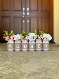 four pink vases with flowers in them sitting on the ground next to a door